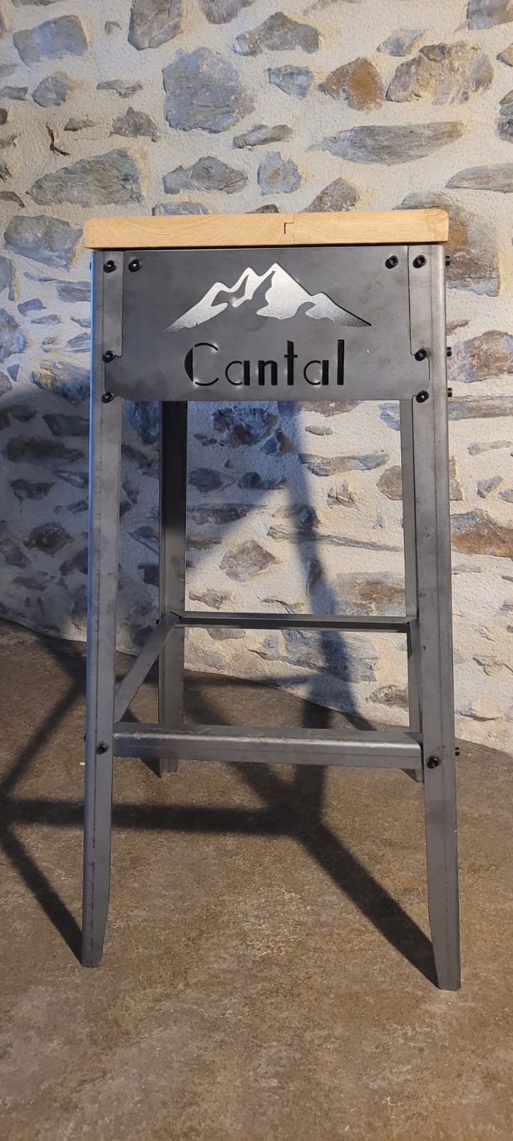 Tabouret haut de style industriel personnalisé avec un logo 'Cantal' et des montagnes découpés au laser, pour un agencement thématique.