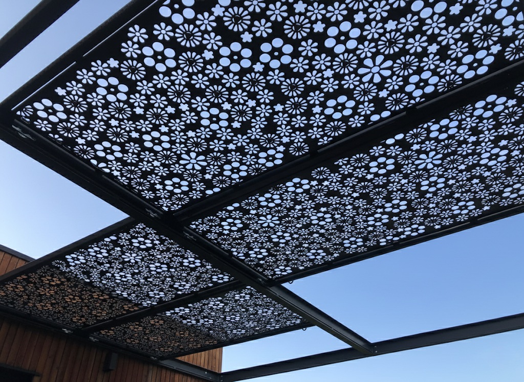 Plafond d'une pergola design sur mesure, composé de panneaux en métal noir avec un motif floral découpé au laser, créant un jeu d'ombre et de lumière.