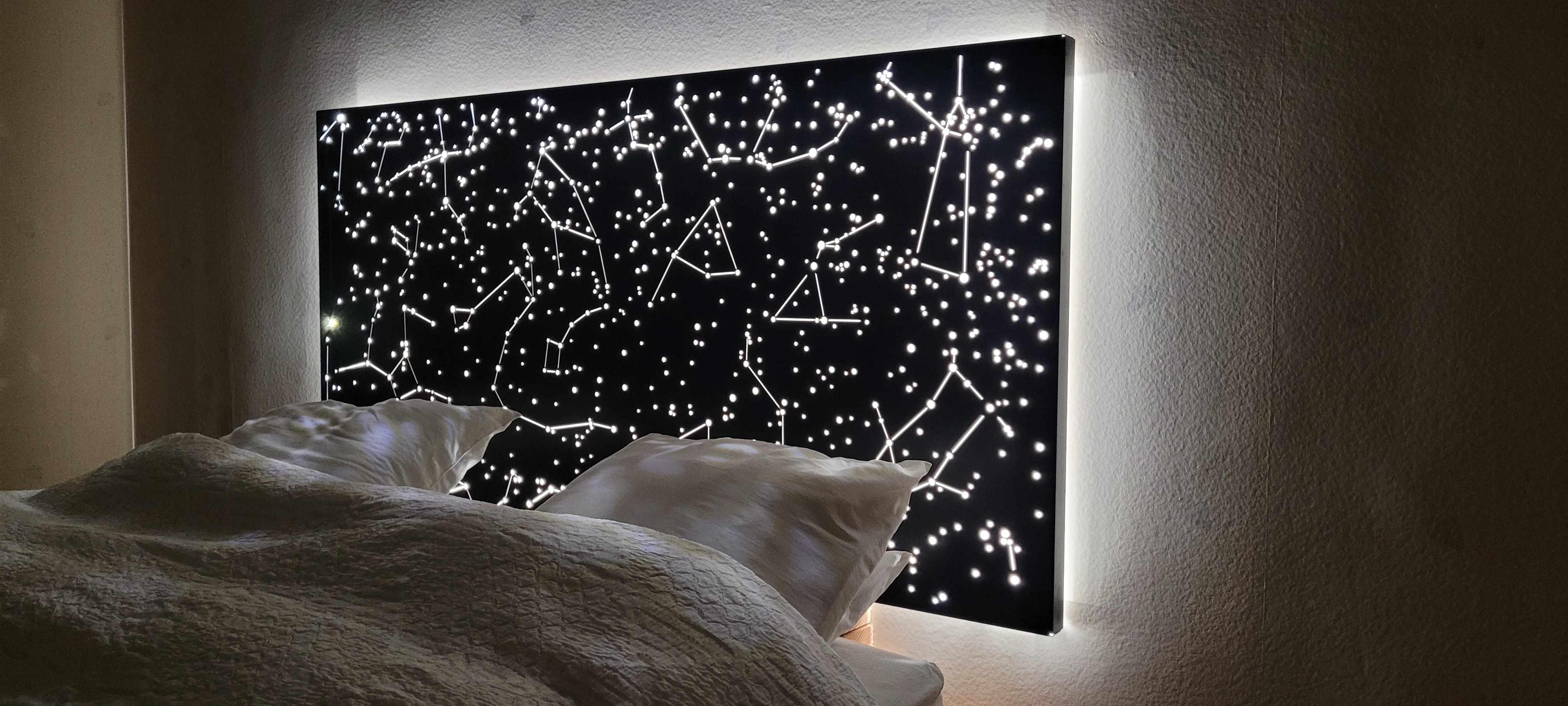 Tête de lit design sur mesure 'La tête dans les étoiles', installée dans une chambre et créant une ambiance de rêve grâce à son rétroéclairage LED qui dessine la carte du ciel.