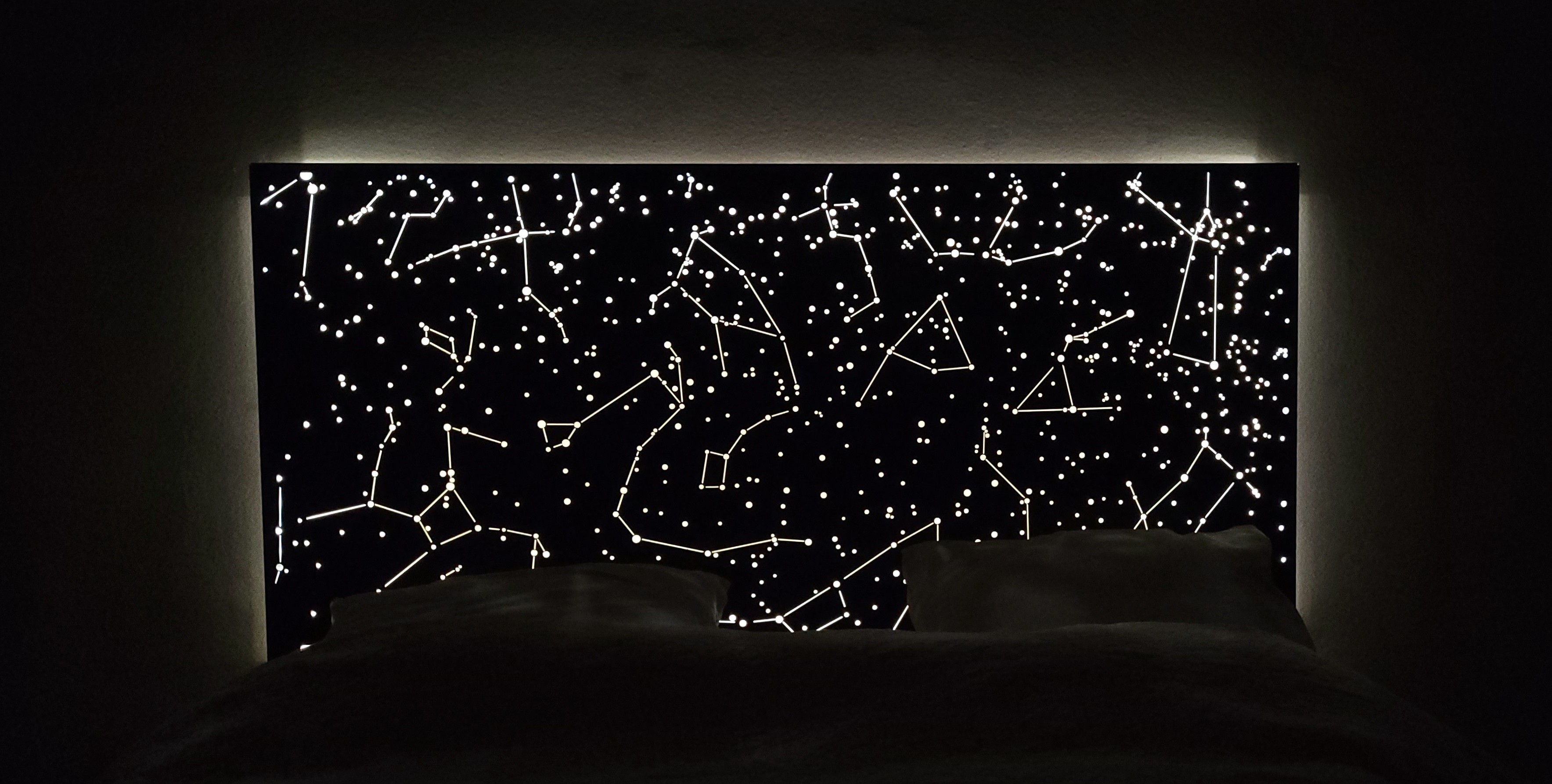 Tête de lit design sur mesure 'La tête dans les étoiles', installée dans une chambre sombre et créant une ambiance intime et onirique grâce à son rétroéclairage LED.
