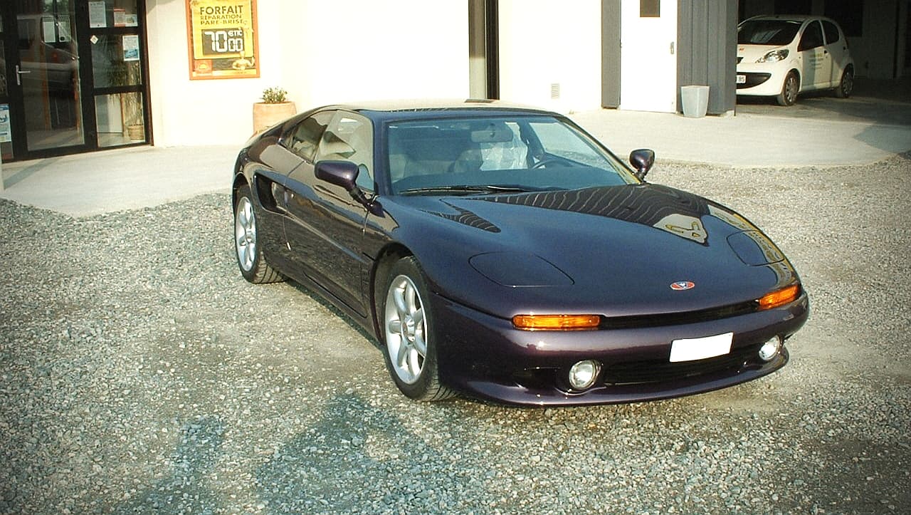 Voiture de sport Venturi 300 violette restaurée stationnée devant un atelier mécanique.