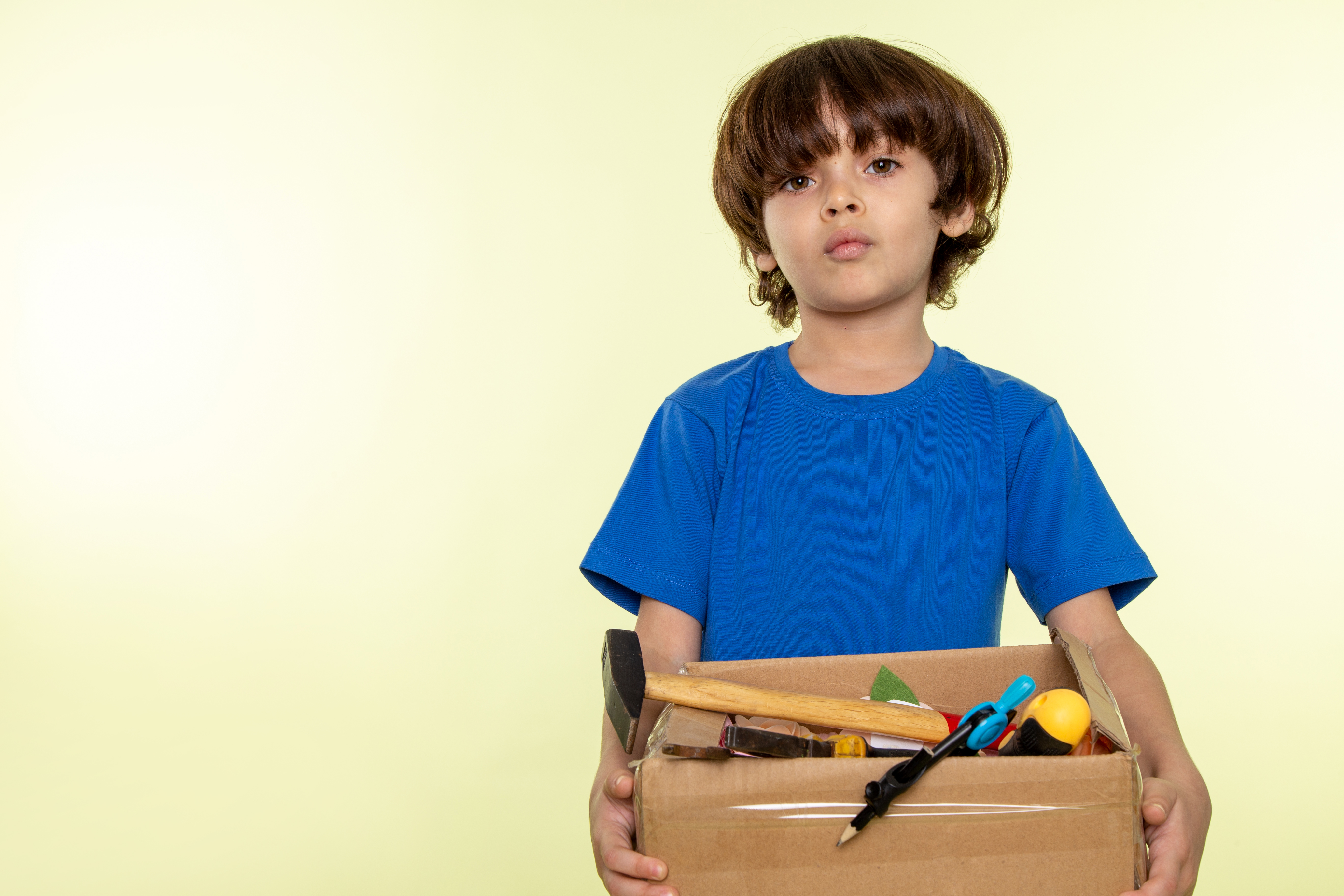 Mignon-garcon-en-bleu-t-shirt-tenant-la-boite-avec-des-outils-sur-le-mur-blanc