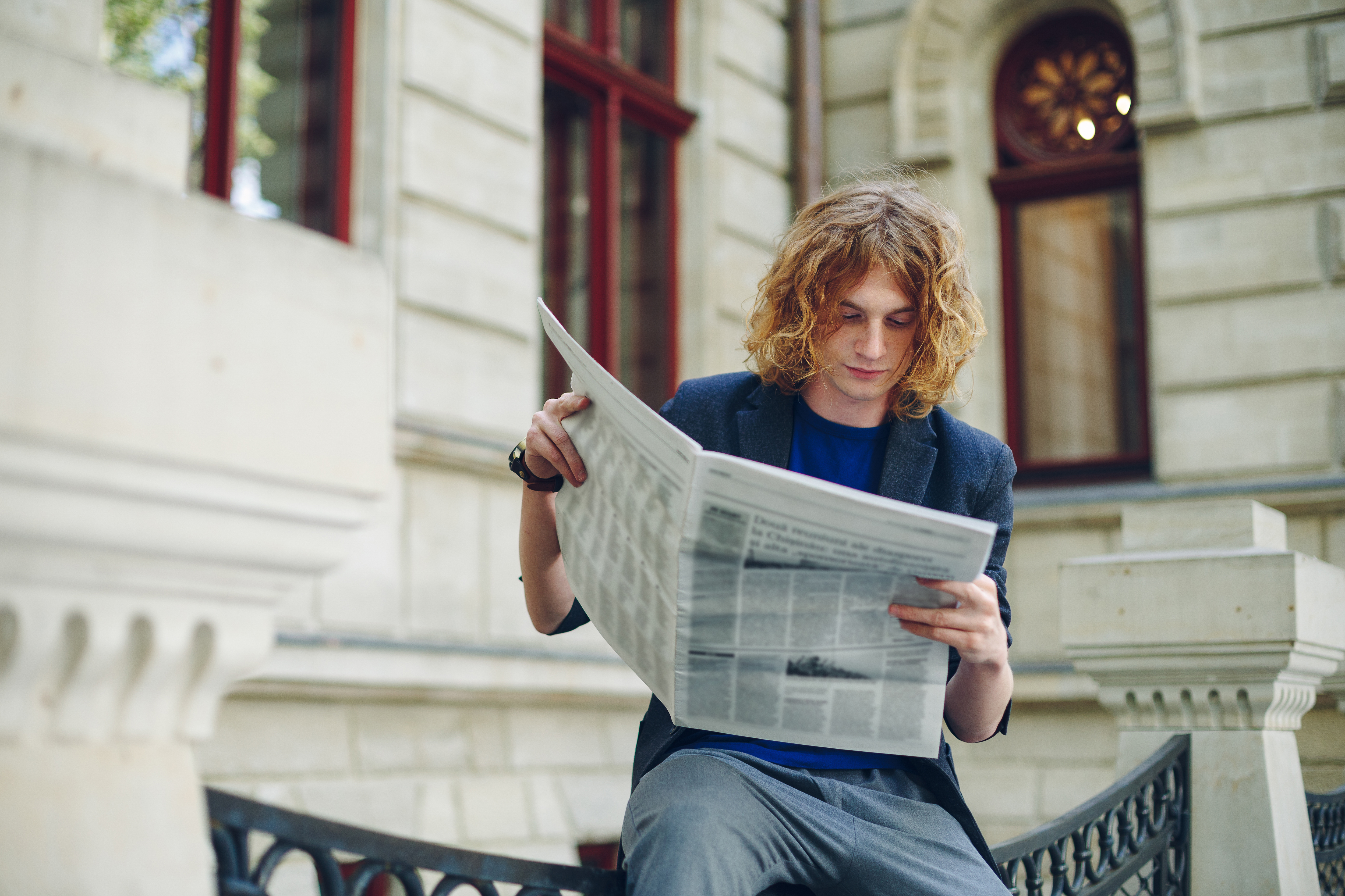 Young-reddish-man-reading-newspaper-near-old-style-building