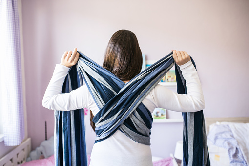 Beautiful young mother wrapping sling for baby around her picture id614208830