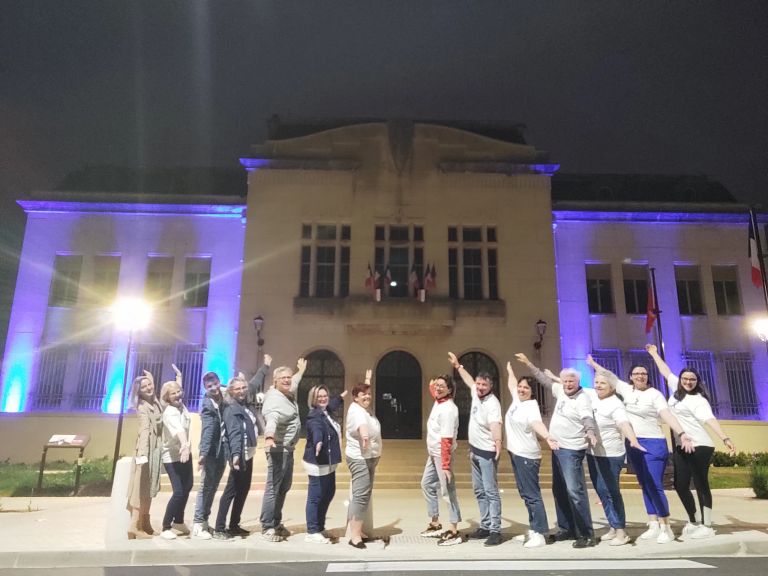 Les adhérents de l'association Fibromyalgie Aube devant l'hôtel de ville de Saint-Julien-les-villas éclairé en bleu pour la journée mondiale de la Fibromyalgie.