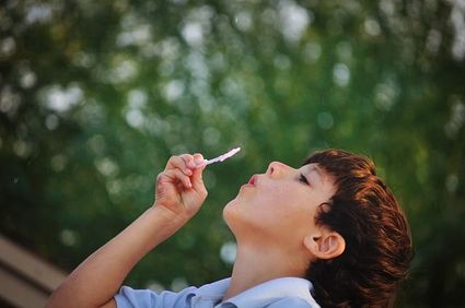 Cette image est une photo d'un garçon de 8 ans environ, la tête penchée en arrière, en train de souffler dans son jeu pour faire des bulles. Cette image inspire le calme, l'amusement, la simplicité.