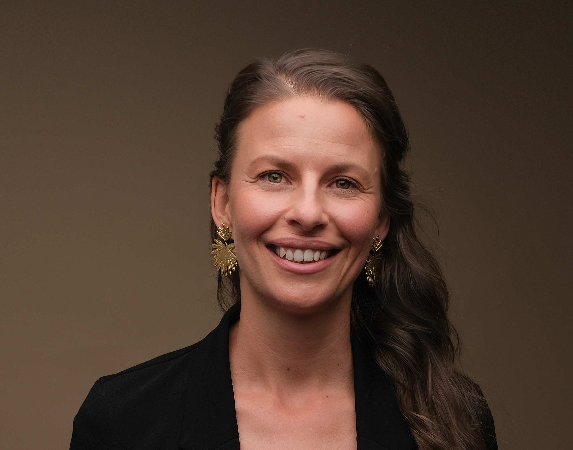 Cette image est une photo portrait de Juliette Cazor, sophrologue enfants, sophrologue adolescents, ambassadrice mon moment magique, animatrice d'ateliers collages. Souriante, des grosses boucles d'oreilles dorées, les cheveux longs attachés à mi hauteur tombant sur l'épaule gauche. 