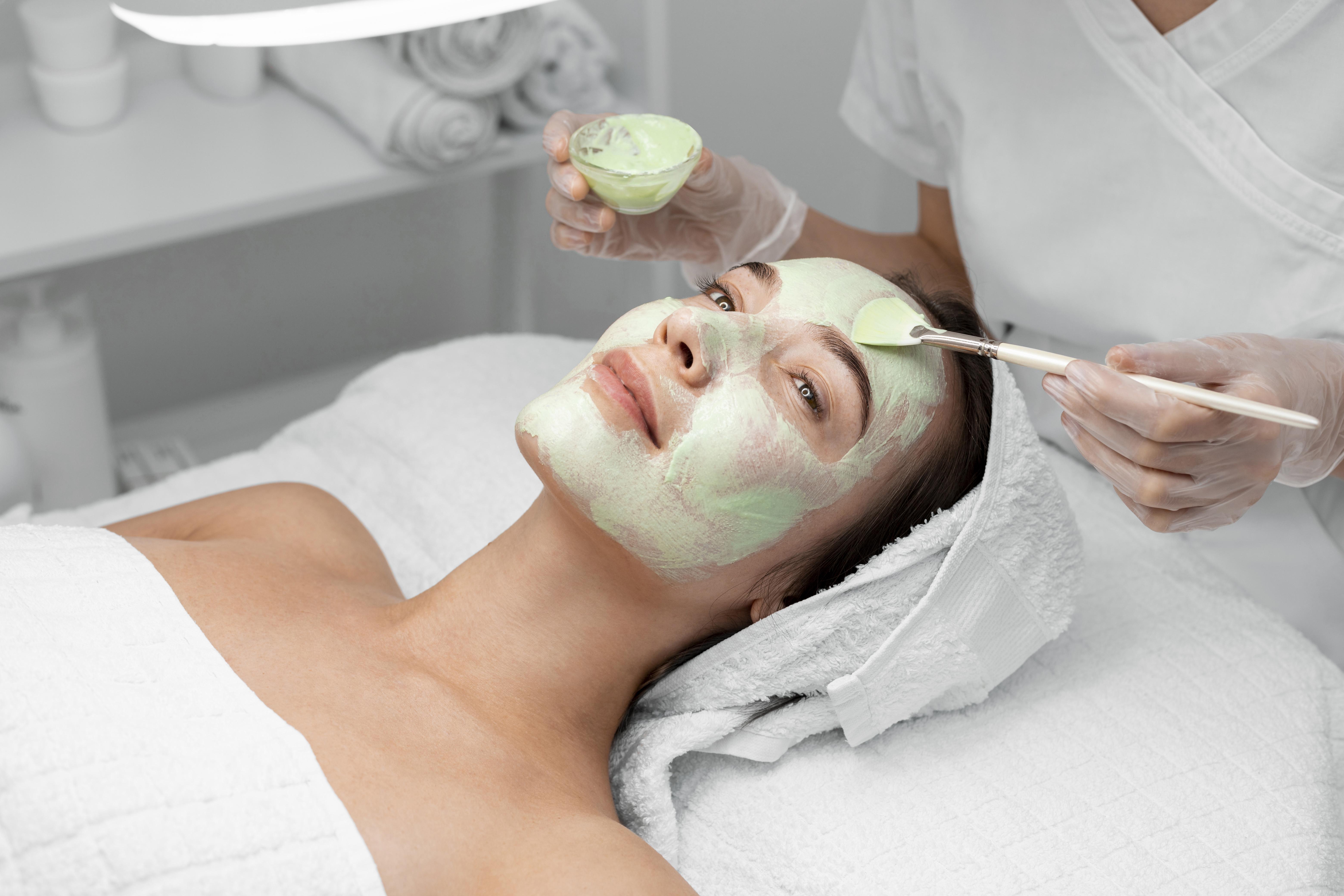 Beautician-applying-face-mask-female-client