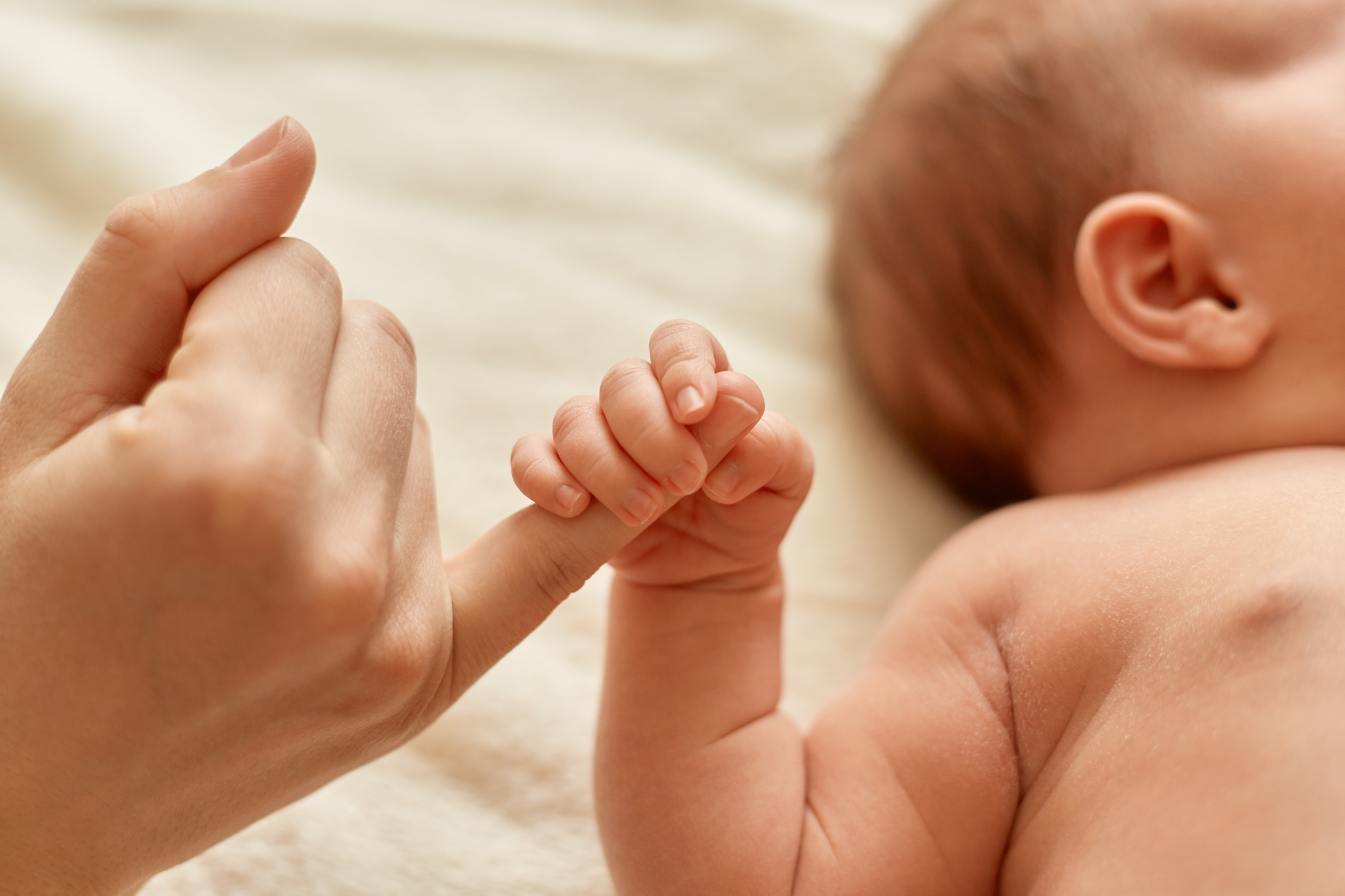 Faceless mother with naked baby infant holding mommy s finger mum spending time with her tiny child light background