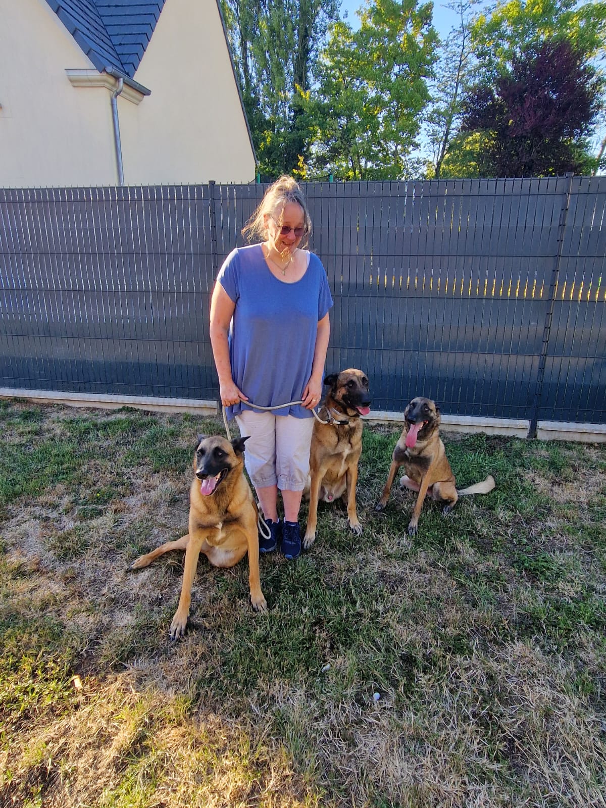 Karine Bigot, éducateur canin en Seine-et-Marne (77), avec trois Malinois : sa chienne, son fils et une femelle de la même portée, chez les propriétaires — moment de retrouvailles familiales.