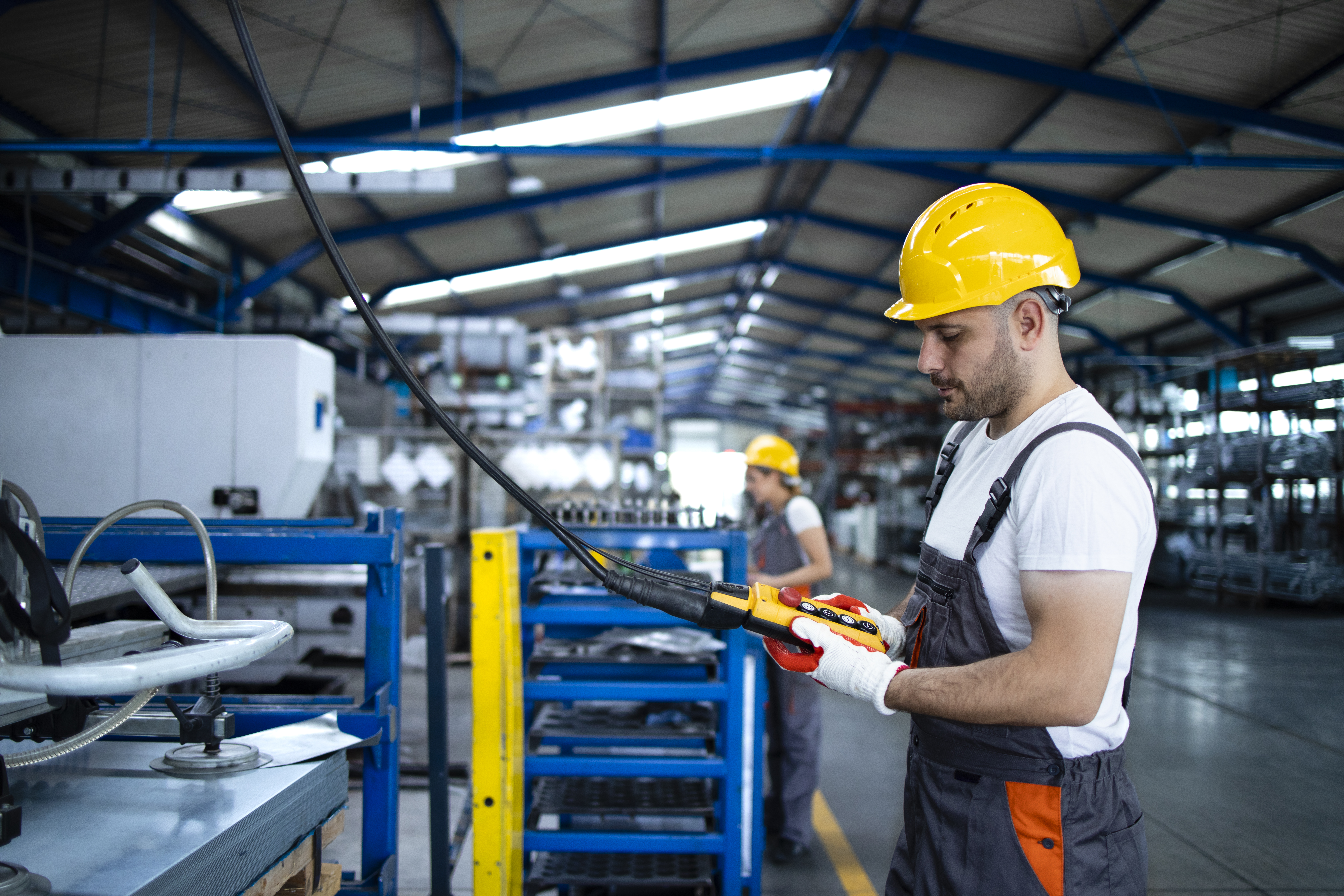 Ouvrier d usine portant l uniforme et la machine industrielle d exploitation de casque avec manette de commande dans le hall de production