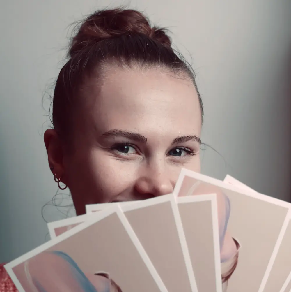 Photo protrait d'une jeune femme tenant en éventail des cartes devant elle cachant une partie de son visage.