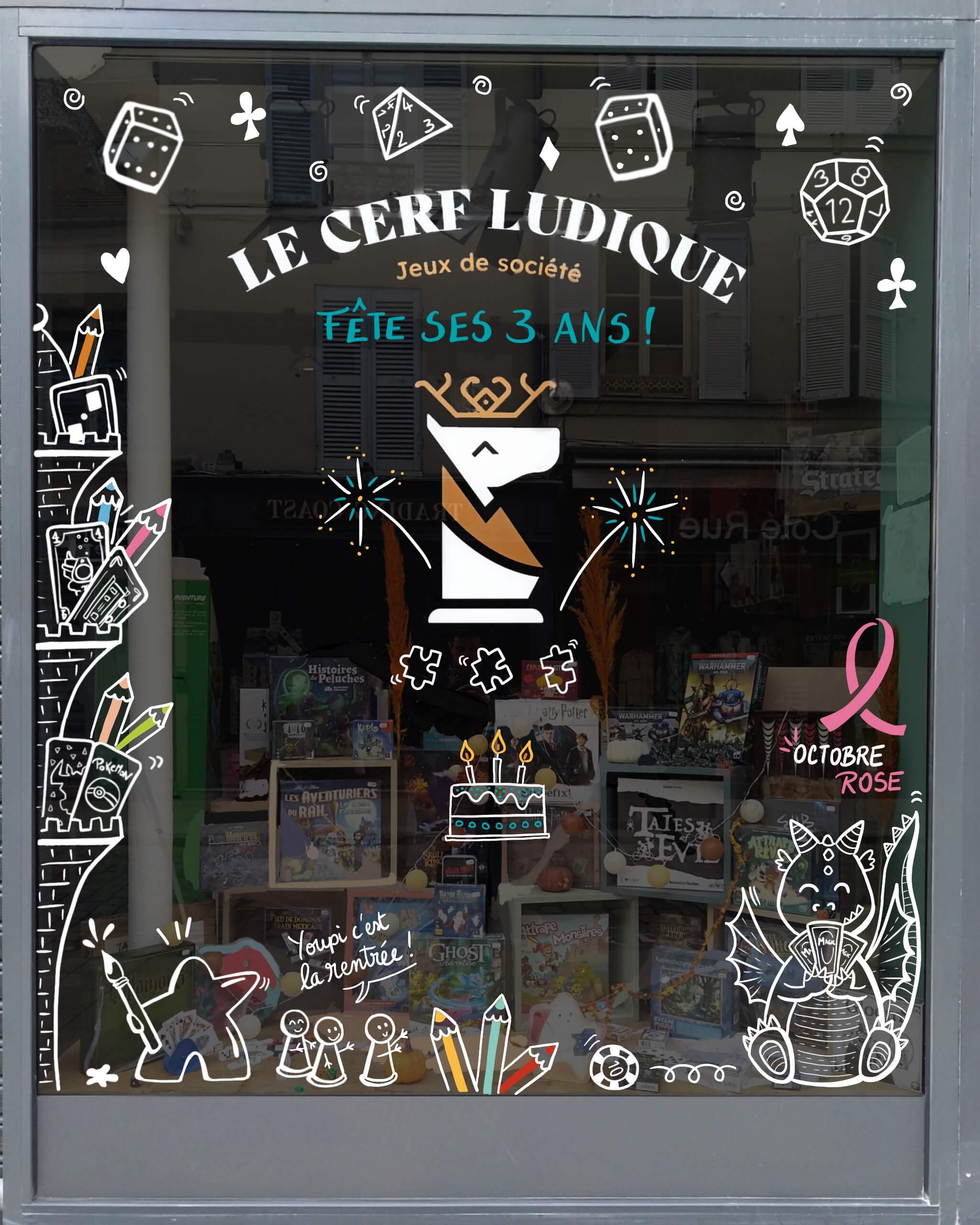 Décor de vitrine pour la boutique Le Cerf Ludique à Rambouillet sur le thème des jeux, avec également un thème de rentrée, l'anniversaire des 3 ans du magasin et Octobre Rose.