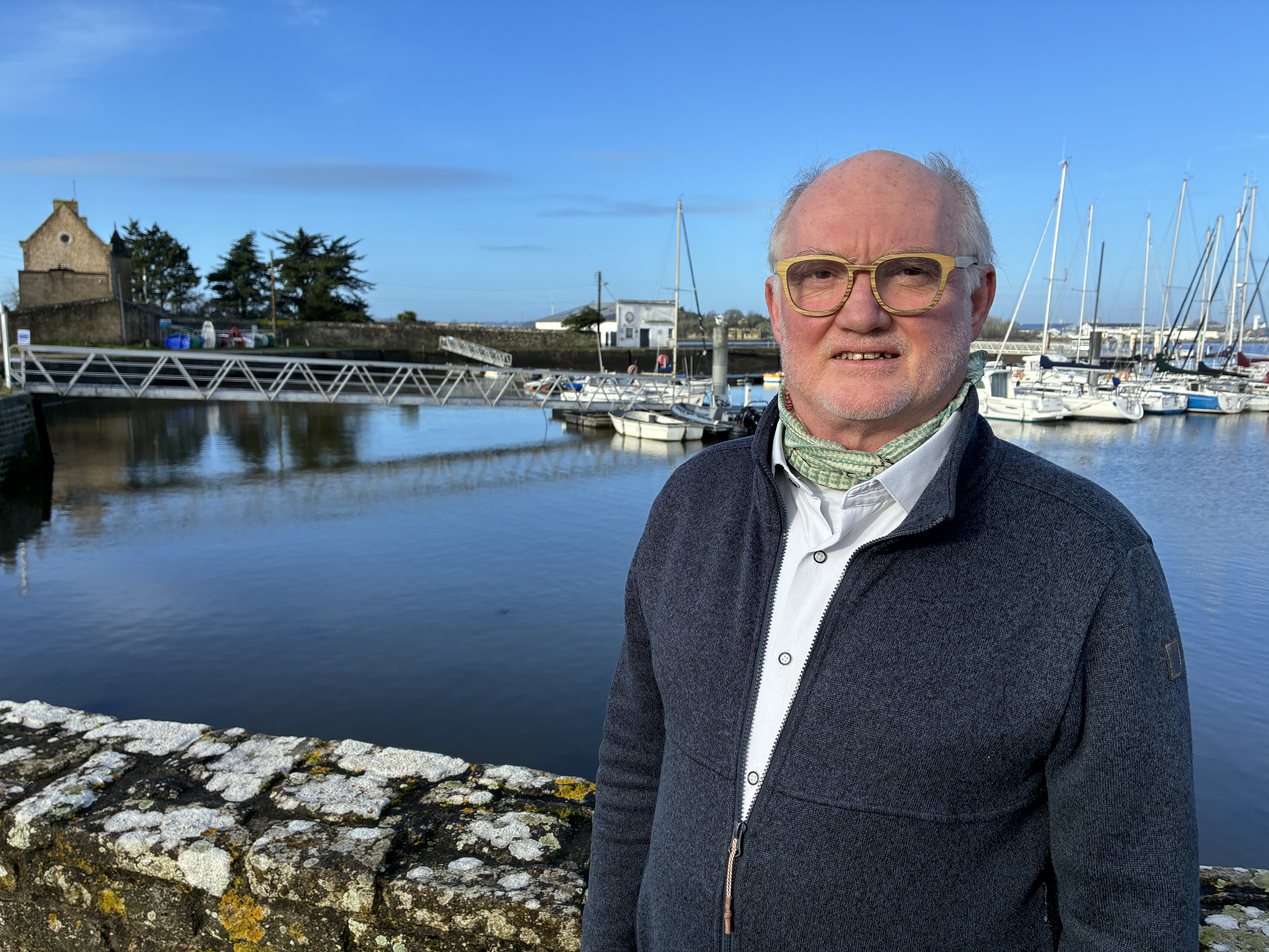Photo de Marc Geourjon, devant le port de Sainte-Catherine, le batîment de la SNSM en arrière-plan. Il fait beau, le ciel est bleu et la mer calme.