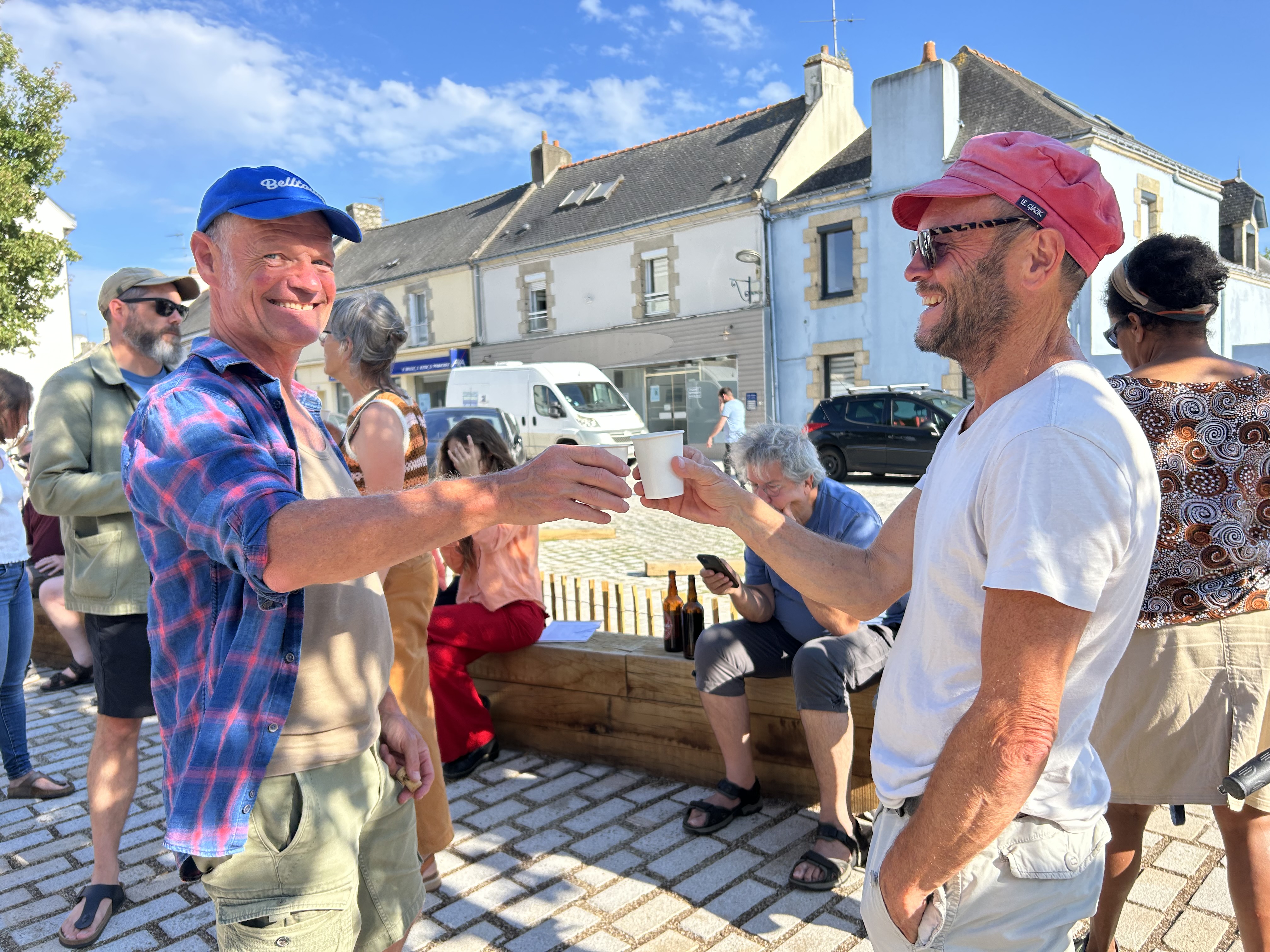 Devant le coccimarket, apéro participatif, 2 personnes trinquent au premier plan.