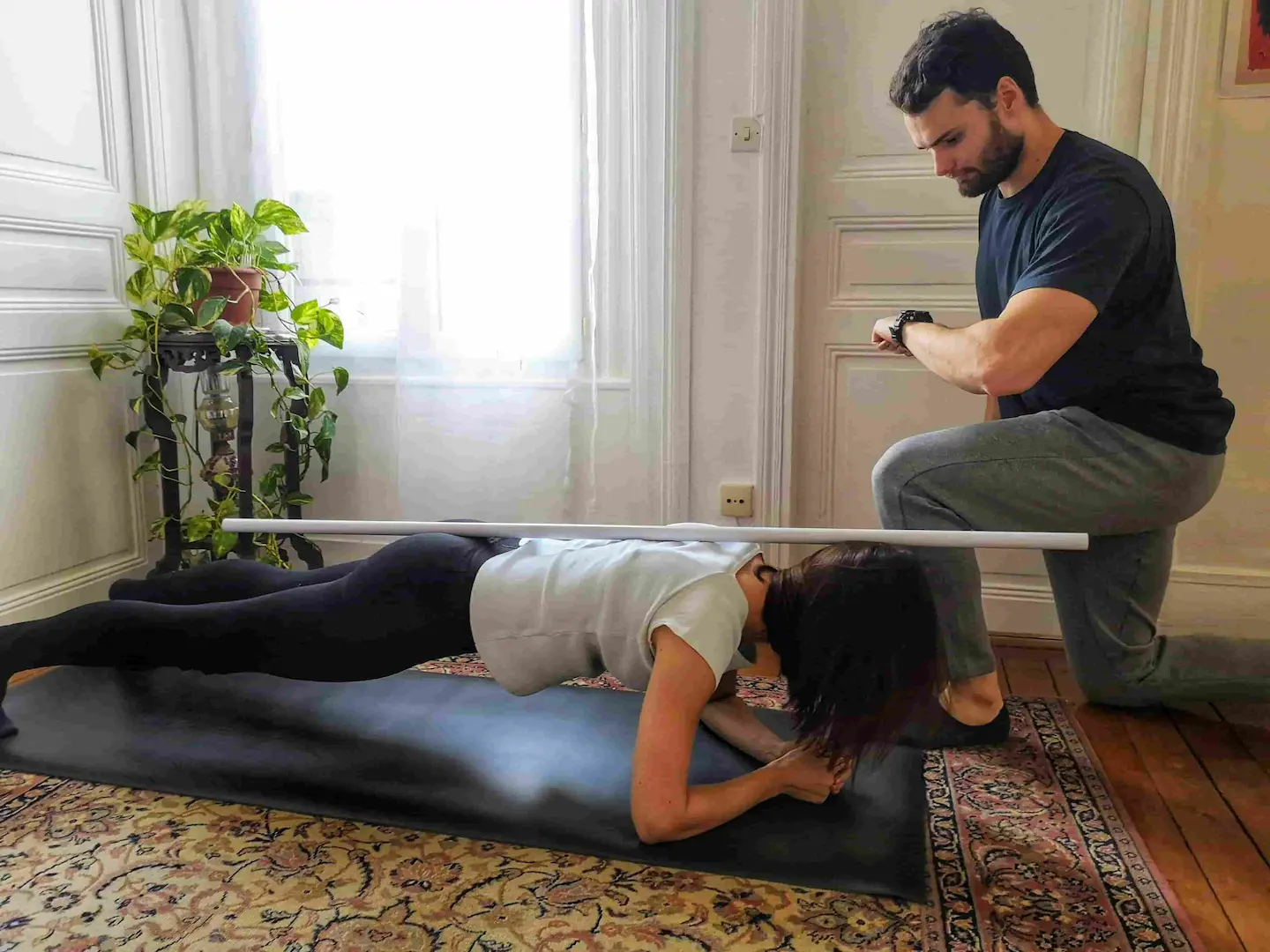 Alexis Glomeron, coach sportif à domicile Paris 6e, supervise un exercice de gainage avec barre de posture dans un appartement haussmannien