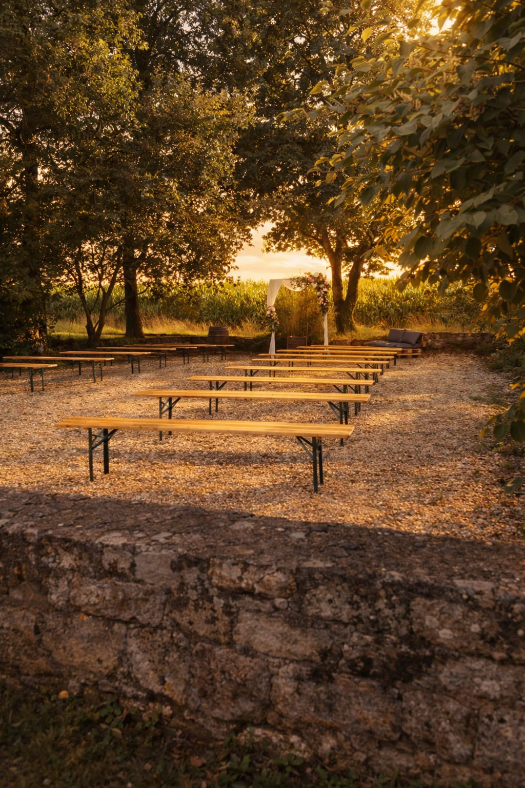 Cérémonie en extérieur sous les arbres, avec arche fleurie et bancs en bois