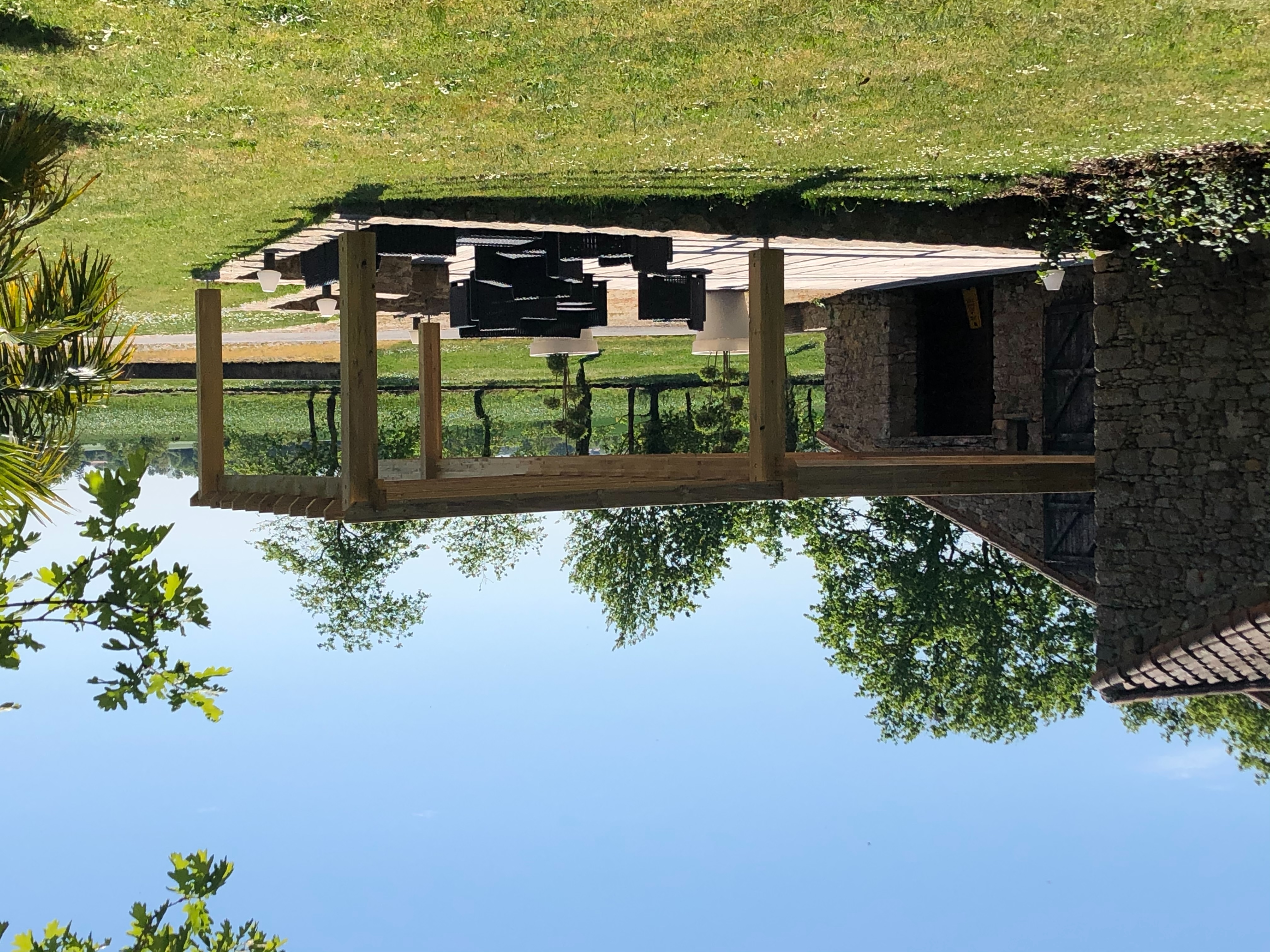 Terrasse en bois sous pergola devant la façade en pierre du domaine