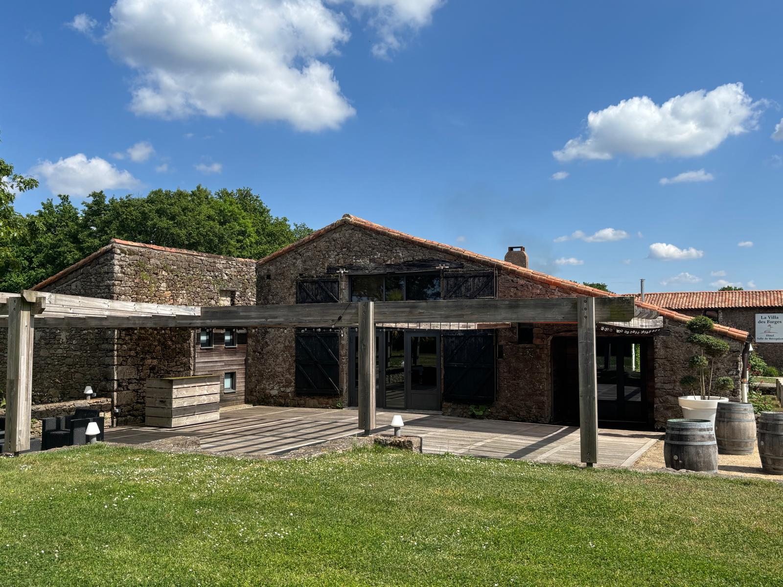 Terrasse en bois sous pergola devant la façade en pierre du domaine