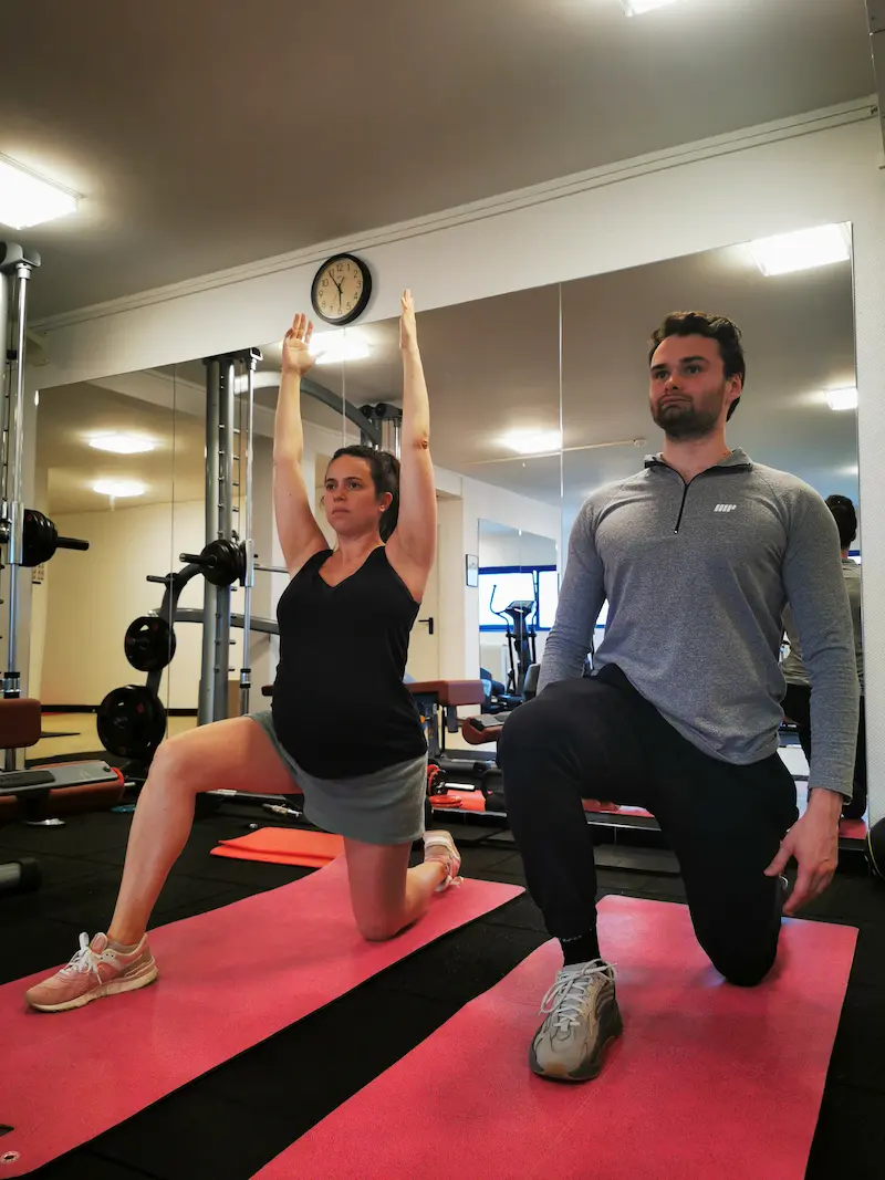 Méthode de coaching maternité à Paris — fente avant en mobilité guidée par Alexis Glomeron en démonstration côte à côte avec une cliente enceinte