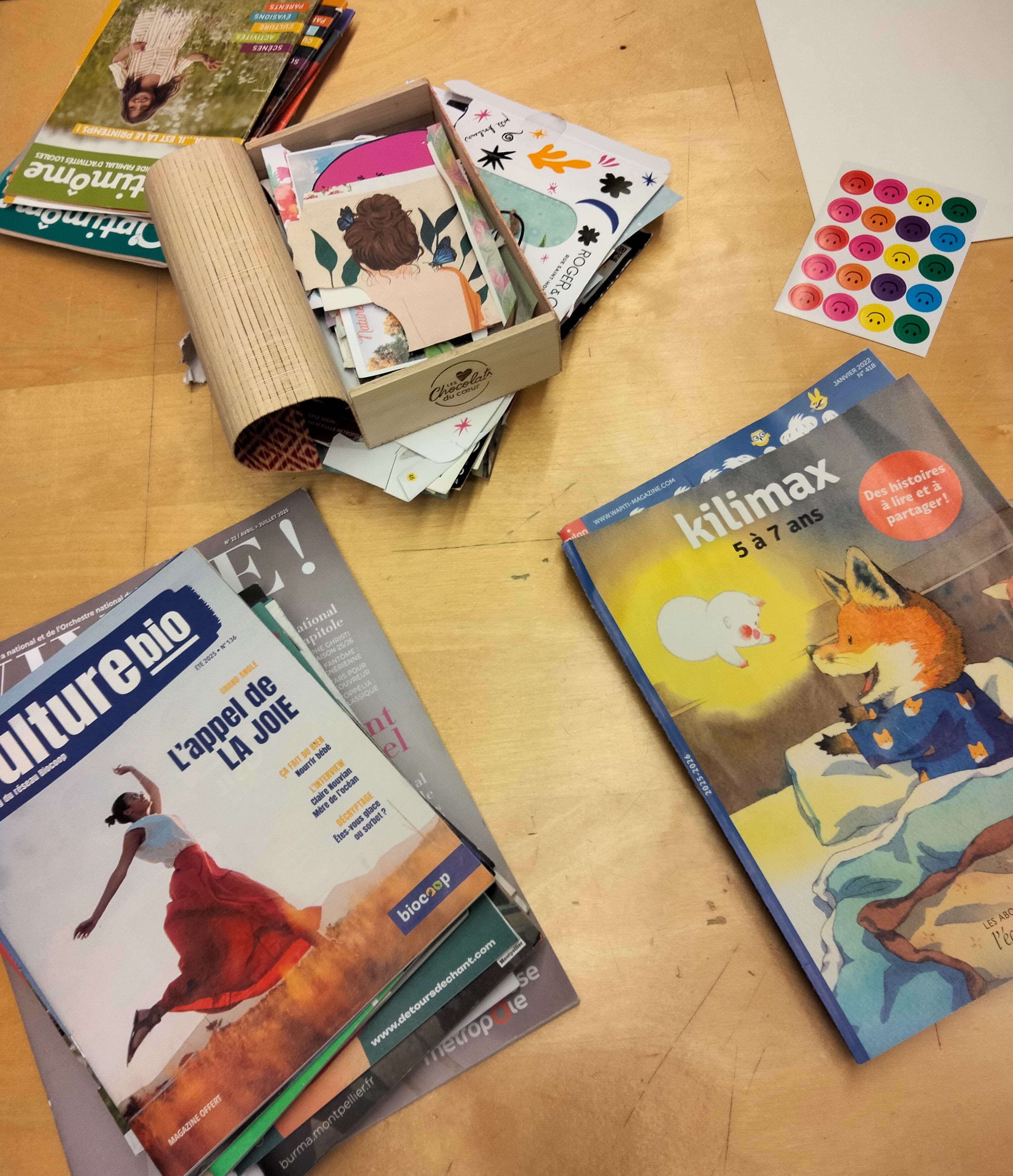 Cette image représente deux piles de magazines et une boîte contenant des images découpées.