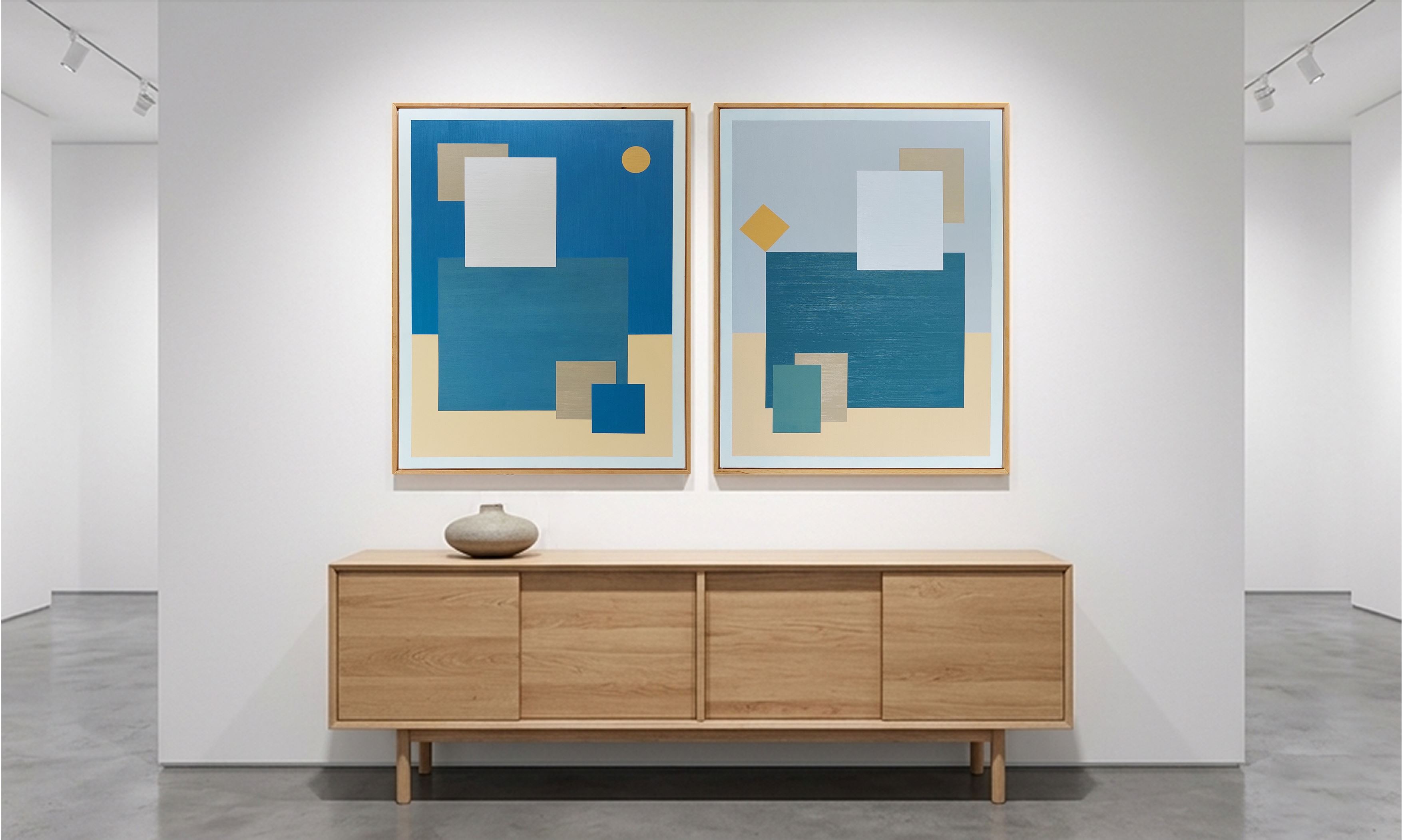 Vue d'ensemble du diptyque de tableaux abstraits géométriques encadrés bois par SELESTICA, accrochés côte à côte au-dessus d'un buffet minimaliste en chêne clair avec un vase céramique, dans une galerie d'art moderne au sol en béton poli.
