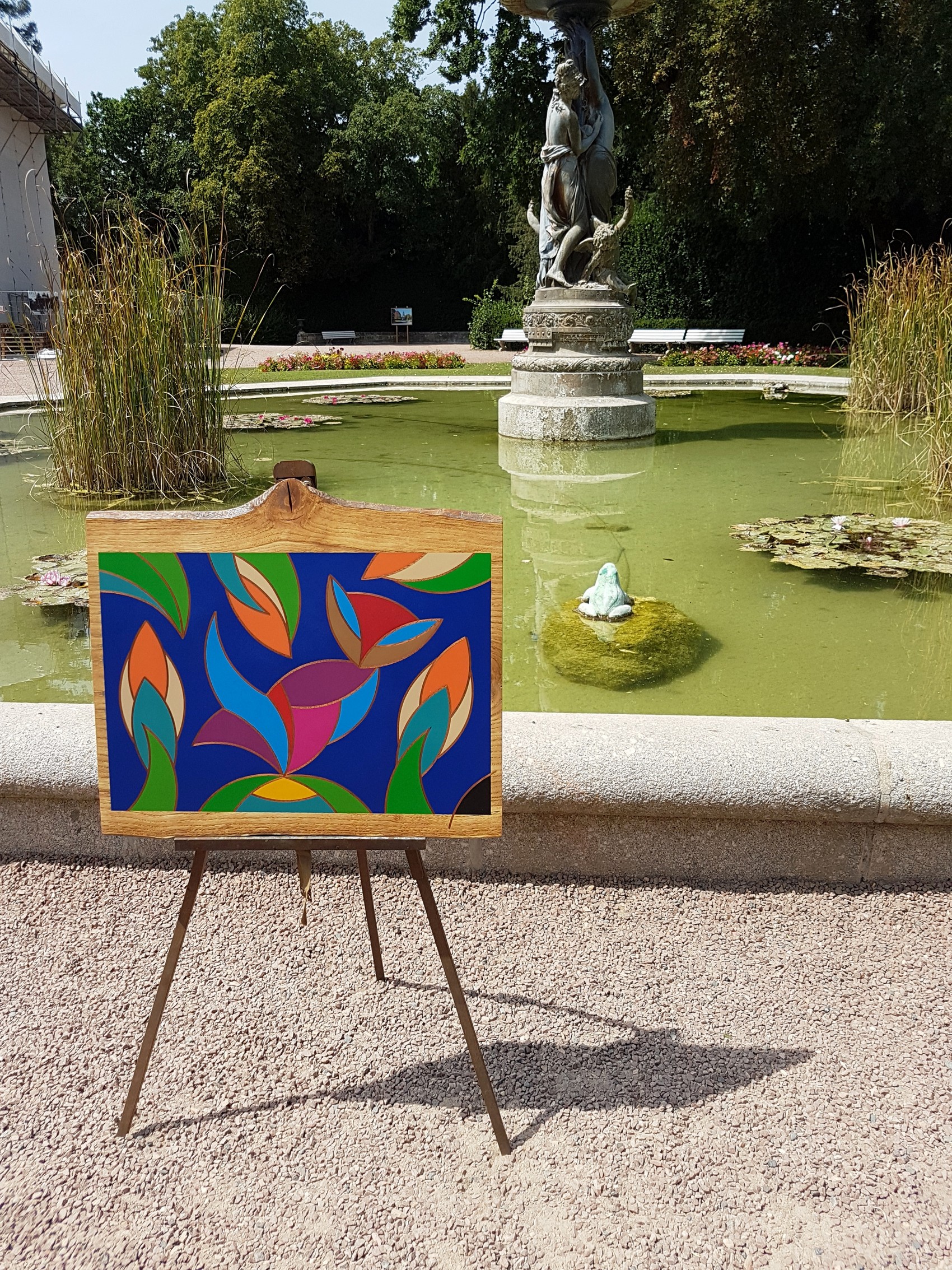 Tableau en cloisonnée de David Vereecken exposé sur un trépied devant une fontaine au soleil.

